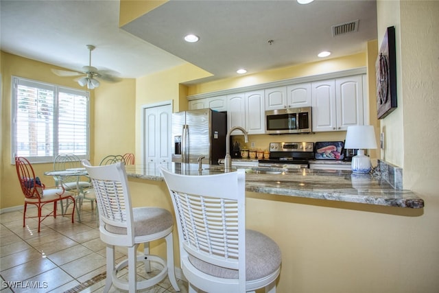 kitchen featuring kitchen peninsula, a breakfast bar, stainless steel appliances, light tile patterned floors, and white cabinets