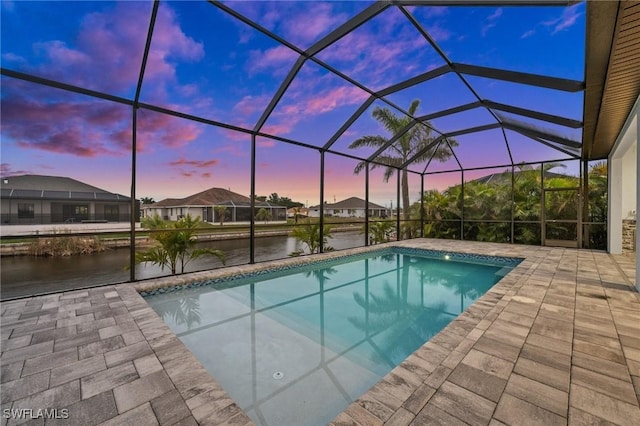 pool at dusk with a patio, a water view, and glass enclosure