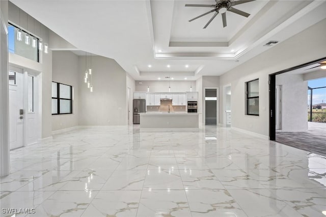 living room with a towering ceiling, a tray ceiling, ornamental molding, sink, and ceiling fan