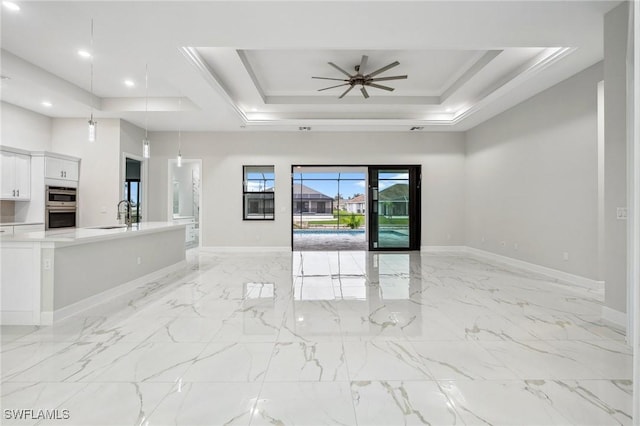 unfurnished living room with a tray ceiling, ornamental molding, sink, a high ceiling, and ceiling fan