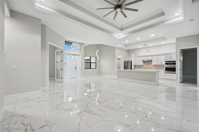 unfurnished living room with sink, a high ceiling, ceiling fan, a raised ceiling, and crown molding