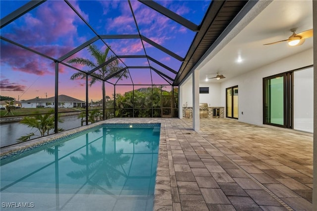 pool at dusk featuring a patio, glass enclosure, ceiling fan, and a water view