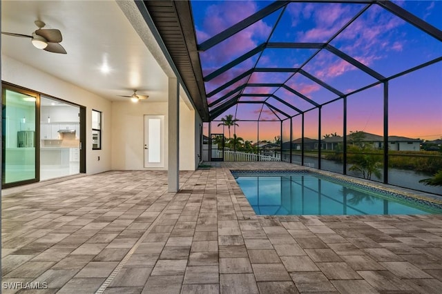 pool at dusk featuring ceiling fan, glass enclosure, and a patio