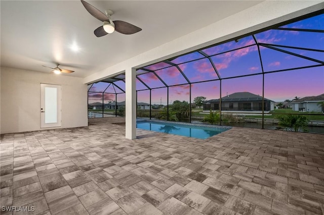 pool at dusk with a patio area, ceiling fan, and glass enclosure