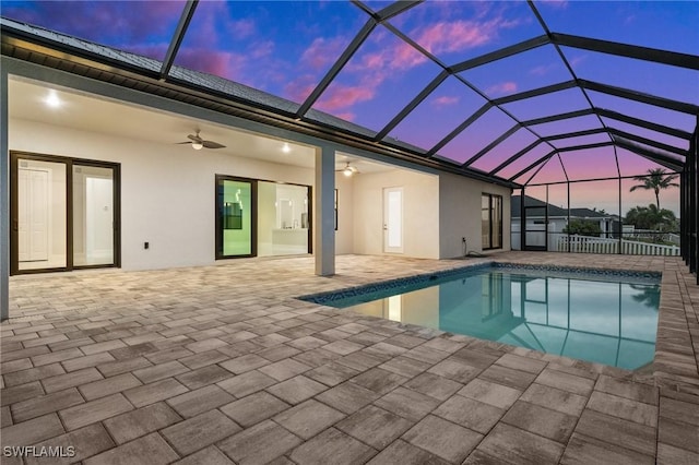 pool at dusk featuring a lanai, ceiling fan, and a patio area