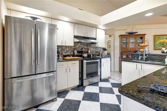 kitchen featuring appliances with stainless steel finishes, backsplash, dark stone counters, sink, and white cabinets