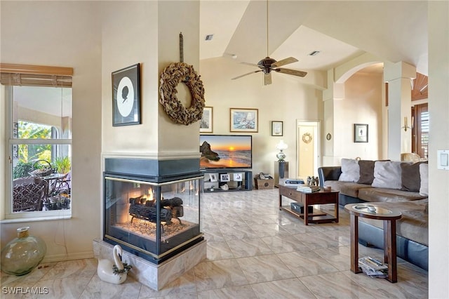 living room with plenty of natural light, ceiling fan, a multi sided fireplace, and high vaulted ceiling