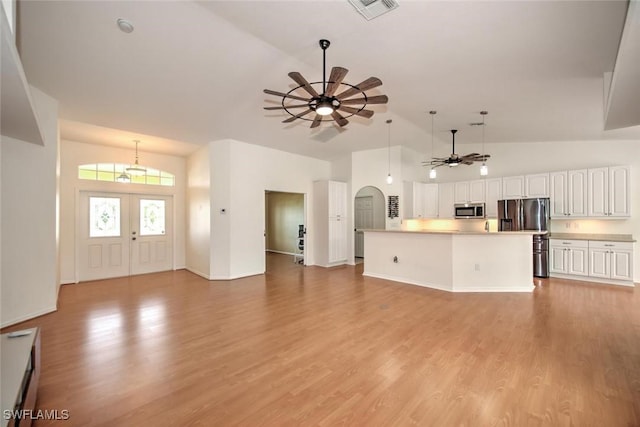 unfurnished living room featuring ceiling fan, light wood-type flooring, high vaulted ceiling, and french doors