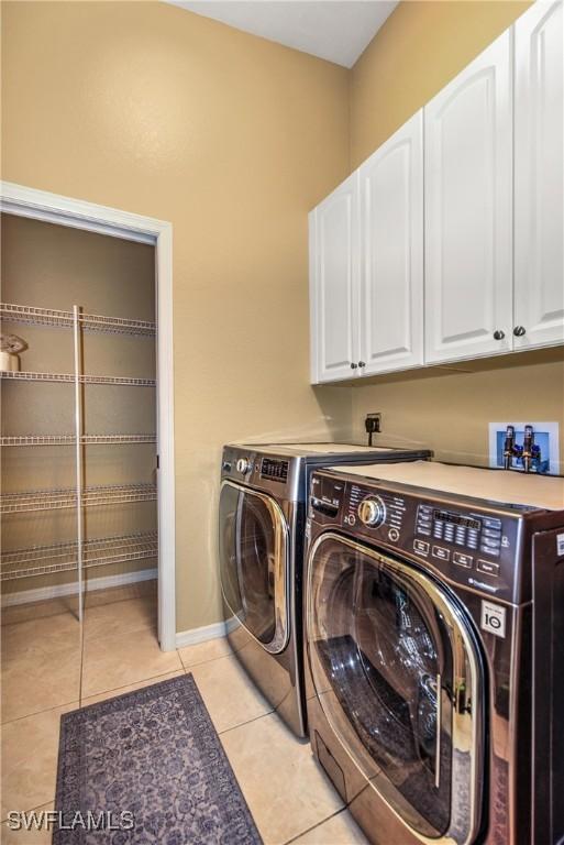 laundry area featuring washer and dryer, light tile patterned flooring, and cabinets