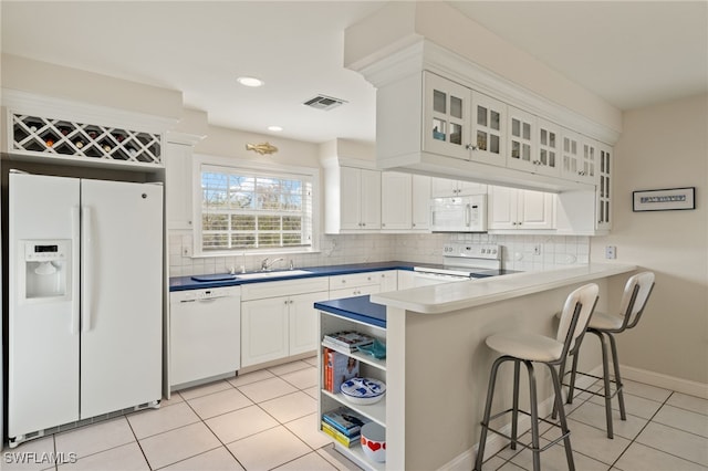 kitchen with white appliances, kitchen peninsula, white cabinets, light tile patterned flooring, and sink