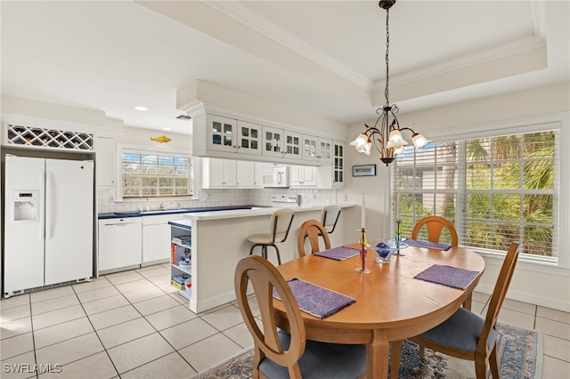 tiled dining room with a raised ceiling, a notable chandelier, crown molding, and plenty of natural light