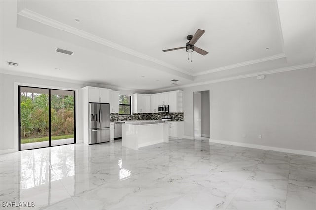 kitchen featuring appliances with stainless steel finishes, a kitchen island, white cabinetry, backsplash, and a tray ceiling