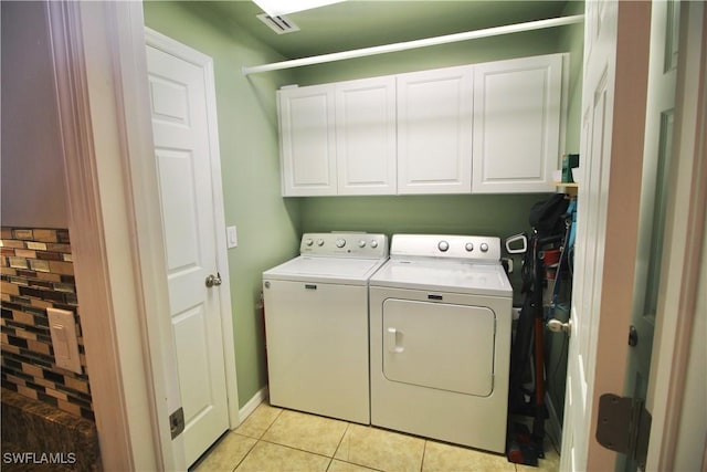 laundry room with washing machine and dryer, light tile patterned floors, and cabinets