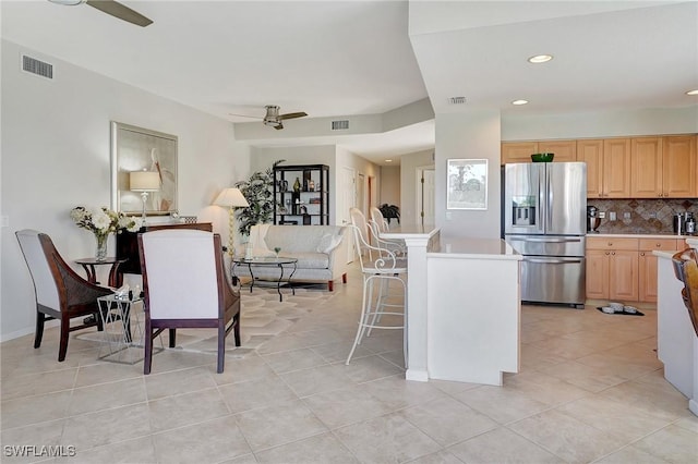 kitchen featuring a kitchen breakfast bar, a center island, light tile patterned floors, stainless steel refrigerator with ice dispenser, and backsplash