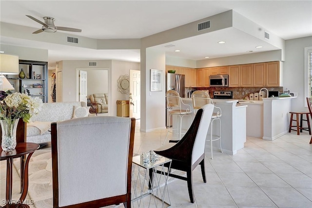 kitchen with decorative backsplash, ceiling fan, a kitchen island with sink, appliances with stainless steel finishes, and light tile patterned flooring