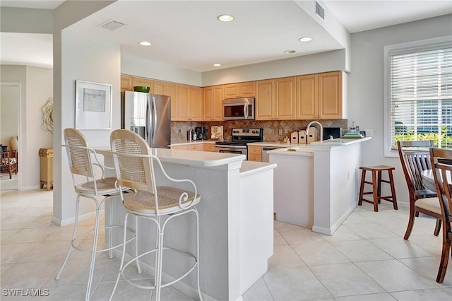 kitchen with kitchen peninsula, stainless steel appliances, light brown cabinetry, and a breakfast bar area