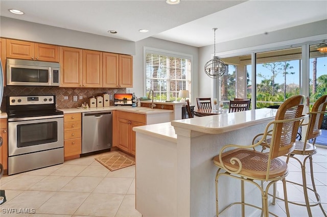 kitchen with a chandelier, appliances with stainless steel finishes, kitchen peninsula, light tile patterned floors, and decorative light fixtures