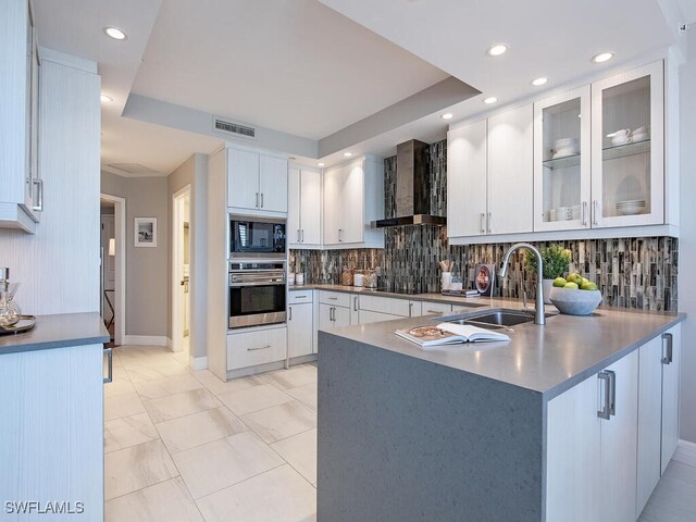 kitchen with kitchen peninsula, sink, black appliances, wall chimney range hood, and white cabinets