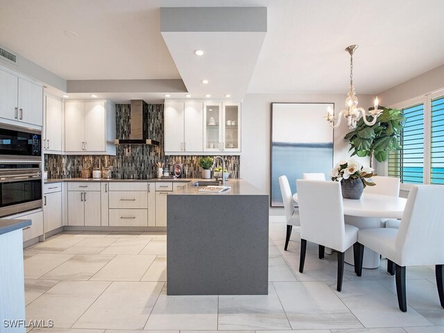 kitchen featuring white cabinets, oven, wall chimney range hood, decorative backsplash, and decorative light fixtures