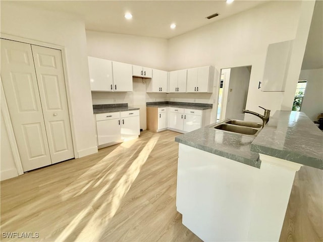 kitchen with light hardwood / wood-style floors, white cabinetry, sink, and a towering ceiling