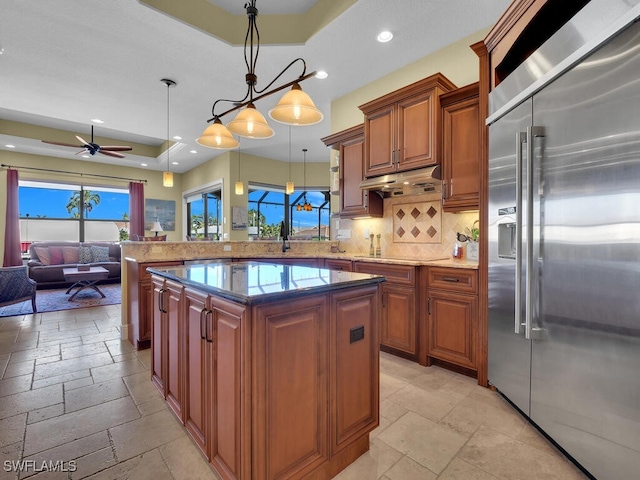 kitchen with decorative light fixtures, decorative backsplash, a tray ceiling, stainless steel built in fridge, and ceiling fan with notable chandelier