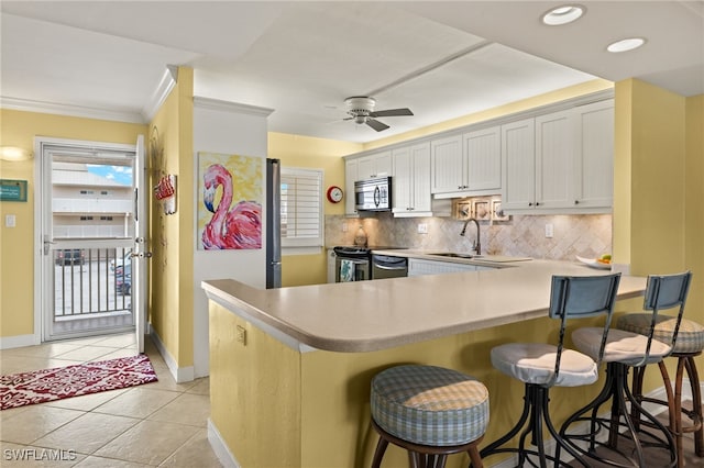 kitchen with a breakfast bar, kitchen peninsula, white cabinets, stainless steel appliances, and backsplash