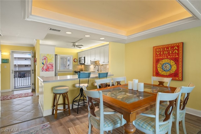 dining space featuring a raised ceiling, ornamental molding, dark hardwood / wood-style floors, and sink