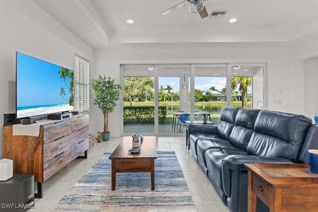 living room featuring a raised ceiling, a water view, light tile patterned floors, and ceiling fan