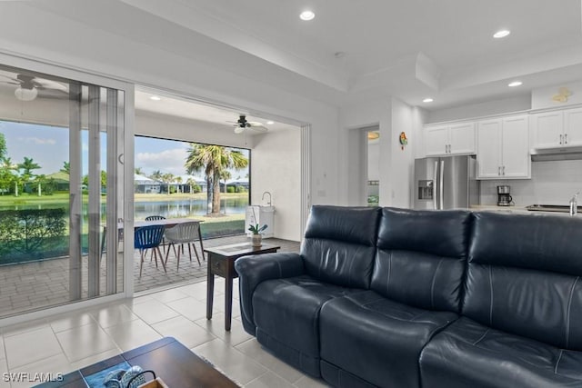 living room featuring ceiling fan, a tray ceiling, a water view, and light tile patterned floors