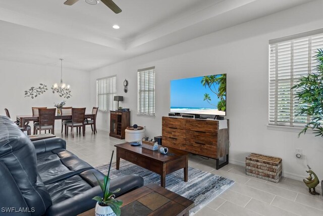 living room featuring a tray ceiling, ceiling fan with notable chandelier, and light tile patterned floors