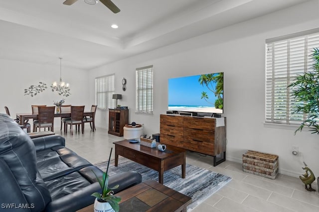 living room with light tile patterned floors, ceiling fan with notable chandelier, and a raised ceiling