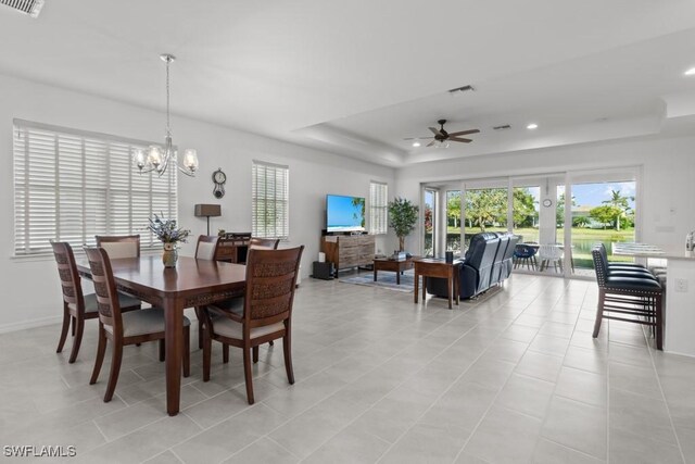 dining space with ceiling fan with notable chandelier, light tile patterned floors, and a tray ceiling