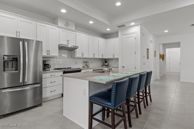 kitchen featuring a center island with sink, appliances with stainless steel finishes, a kitchen breakfast bar, decorative backsplash, and white cabinets