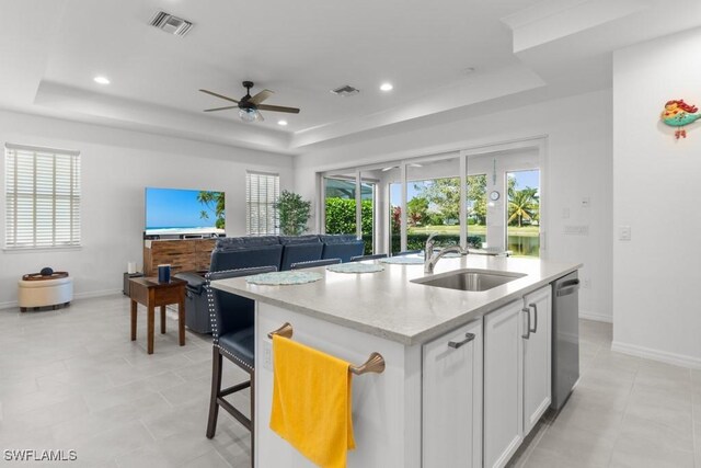 kitchen with sink, white cabinets, an island with sink, stainless steel dishwasher, and a tray ceiling