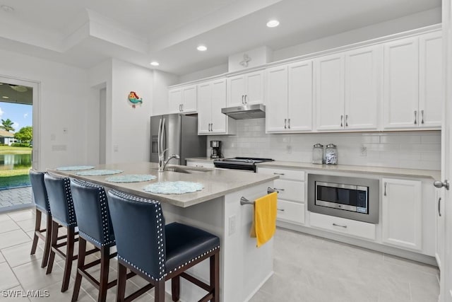 kitchen featuring stainless steel appliances, sink, white cabinetry, tasteful backsplash, and a center island with sink