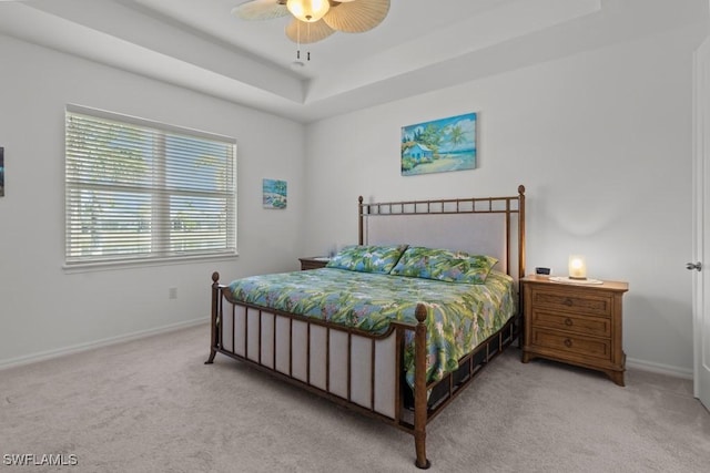 bedroom featuring ceiling fan, light carpet, and a tray ceiling