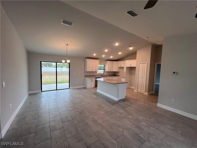 kitchen featuring light stone countertops, vaulted ceiling, a kitchen island, pendant lighting, and white cabinetry