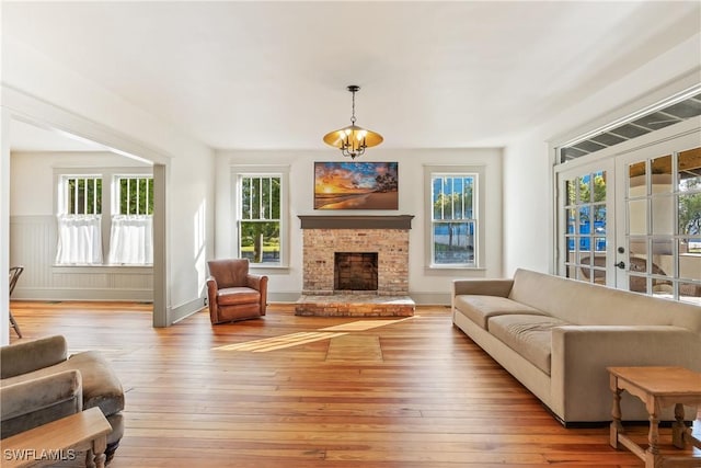 living room featuring a notable chandelier, light hardwood / wood-style flooring, a fireplace, and french doors