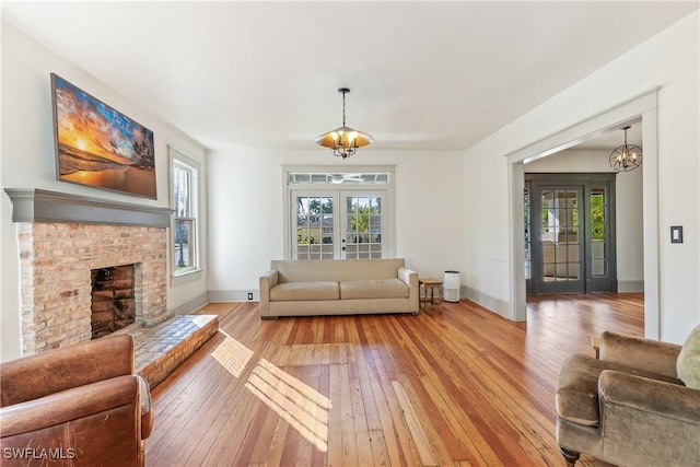 living room featuring a brick fireplace, a notable chandelier, light wood-type flooring, and french doors