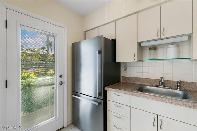 kitchen featuring decorative backsplash, stainless steel fridge, white cabinets, and sink