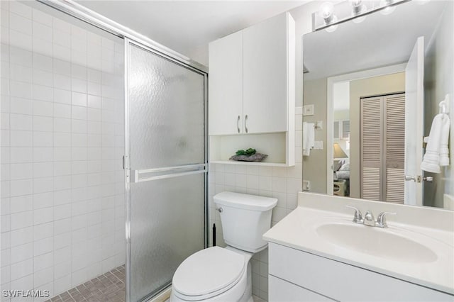 bathroom featuring vanity, toilet, tile walls, and a shower with shower door