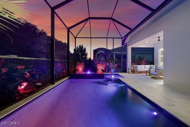 pool at dusk featuring a lanai, outdoor lounge area, ceiling fan, and a patio area