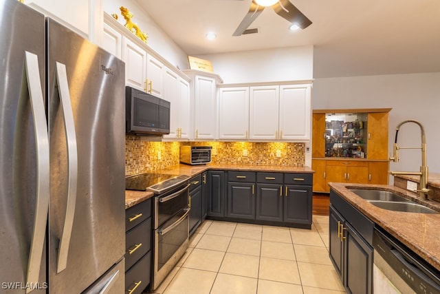 kitchen with dark stone counters, stainless steel appliances, sink, light tile patterned floors, and white cabinets