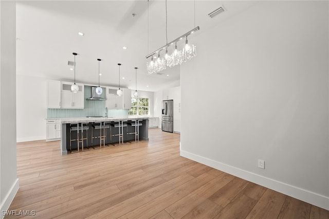 kitchen with a large island, wall chimney exhaust hood, tasteful backsplash, pendant lighting, and white cabinets