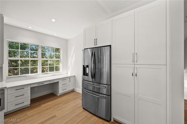 kitchen with stainless steel fridge with ice dispenser, built in desk, light hardwood / wood-style flooring, and white cabinetry