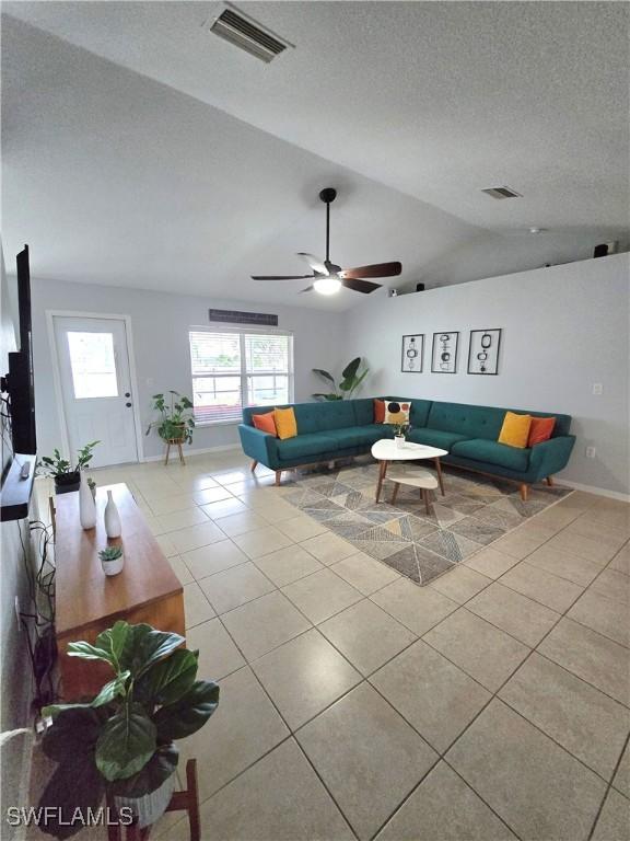 living room featuring vaulted ceiling, ceiling fan, a textured ceiling, and light tile patterned flooring