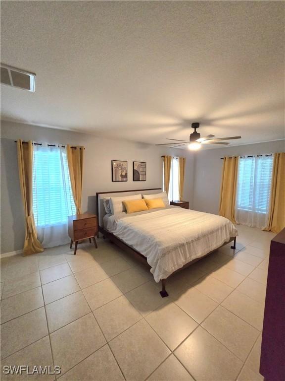 tiled bedroom with ceiling fan and a textured ceiling