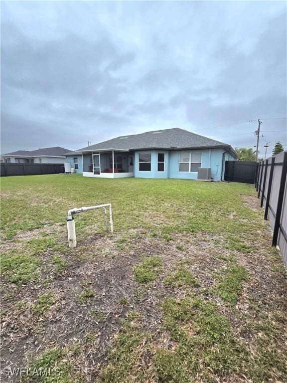 rear view of house with central AC and a yard