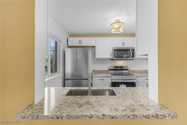 kitchen with light stone counters, a sink, white cabinetry, appliances with stainless steel finishes, and backsplash