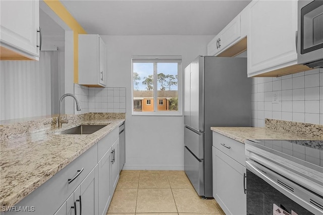 kitchen featuring light tile patterned floors, white cabinets, light stone counters, stainless steel appliances, and a sink